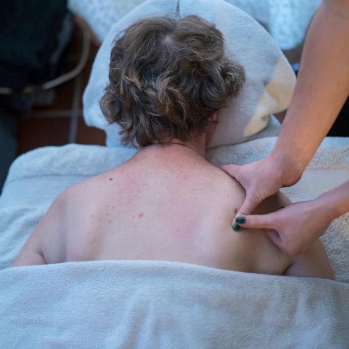 Bovenaanzicht van een persoon op de massagetafel terwijl Joy druk uitoefent op de schouder.