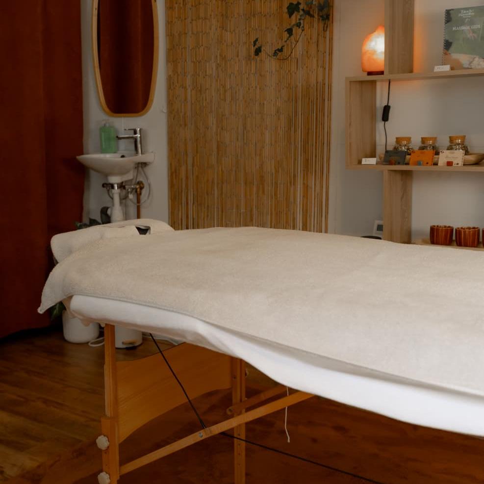 Massageruimte met opgemaakte massagetafel, wasbak en warme sfeerverlichting
